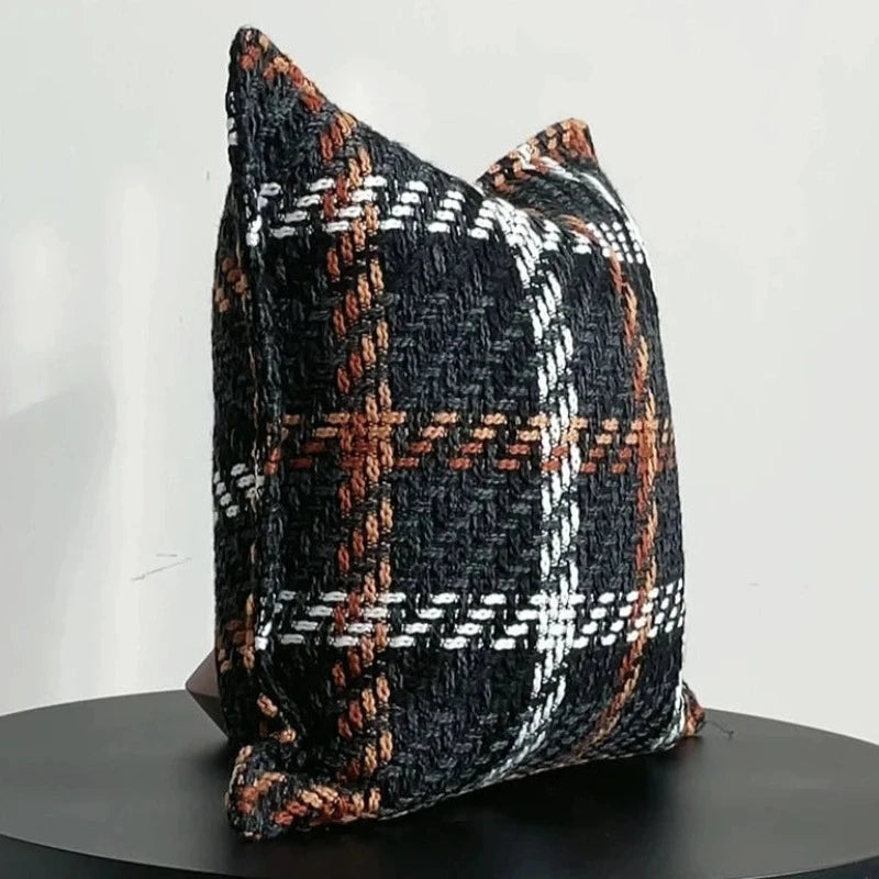 Housse Coussin Carreaux Noir et Blanc texturé avec un motif tartan en noir, blanc, marron, et orange, sur fond blanc - de 3/4 sur table noir