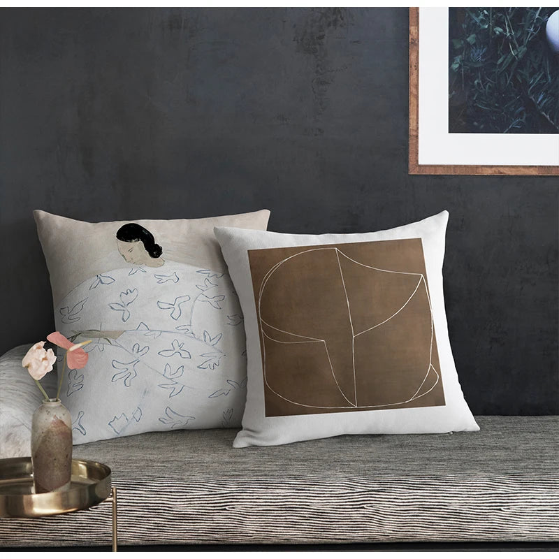 Housse de Coussin Scandinave Ecru Beige Gris Noir décorée d'une illustration artistique représentant une femme aux cheveux noirs entourée de motifs d'oiseaux et de feuilles esquissés en bleu et noir - sur banquette minimaliste sur fond mur noir