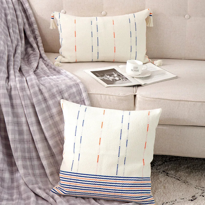 Housse de Coussin Blanc au Crochet avec lignes verticales bleues et orange et bandes horizontales en bas - mis en scène avec canapé taupe et version rectangle