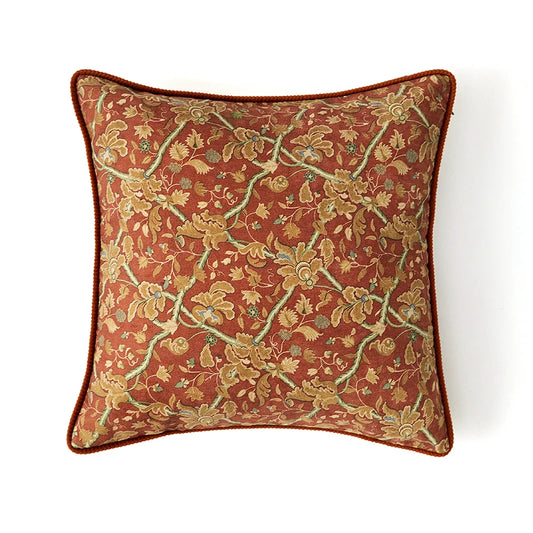 Housse de Coussin Fleurie vu de dessus avec broderies florales dorées et vertes sur un fond rouge brique. Les motifs sont détaillés, les bords arrondis, et une finition en cordon rouge-brun encadre le coussin. Fond blanc pour mettre en valeur le design - de face