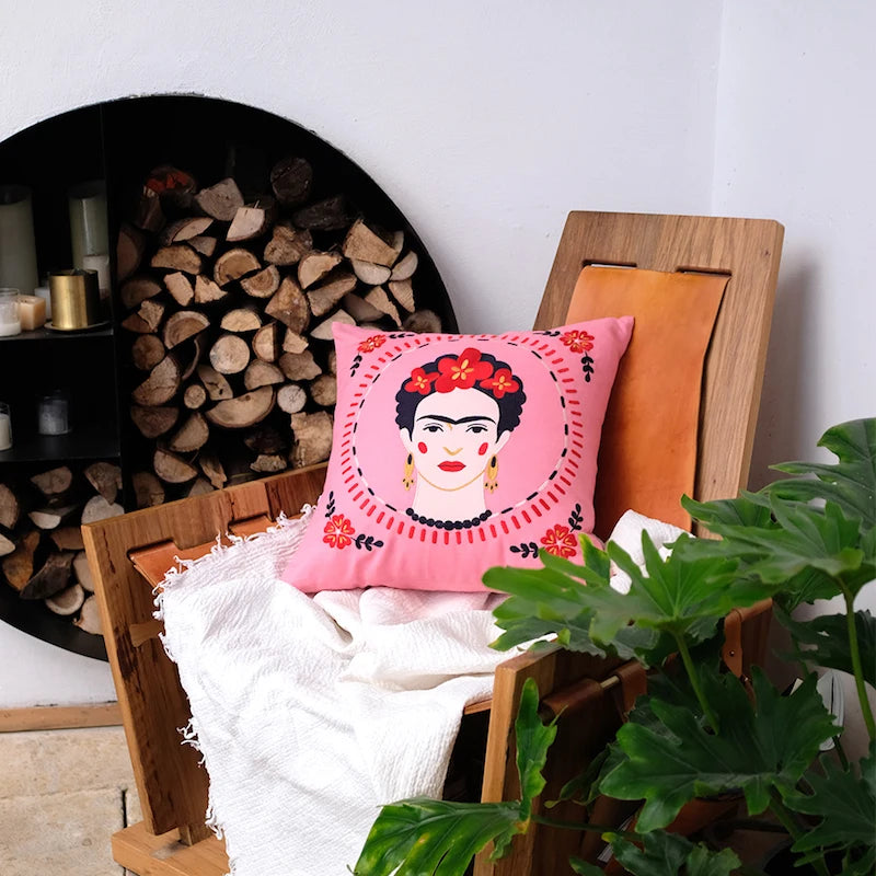 Housse de Coussin 50 x 50 Rose Fushia rose vif avec un portrait stylisé d'une femme, entouré d'une bordure circulaire avec des motifs floraux et des bijoux distinctifs - sur fauteuil en bois et plaid blanc