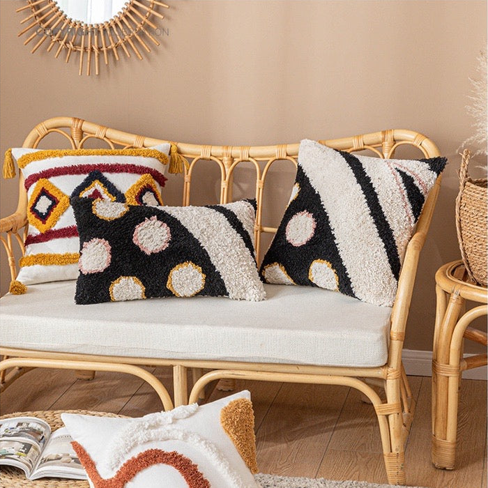 décoratif avec un design abstrait moderne en tissu bouclé, présentant des arcs diagonaux noirs et crème et des cercles beiges et jaunes dans un style audacieux et texturé - sur fauteuil en rotin