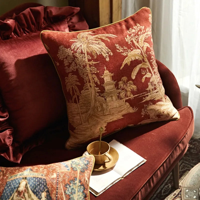 Housse de Coussin Chine Rouge en style asiatique classique avec une pagode entourée de végétation tropicale sur fond rouge bordeaux texturé, motifs dorés raffinés dans un format large - sur canapé rouge