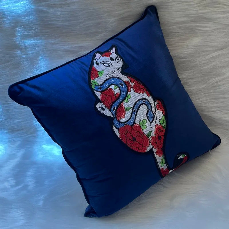 housse de coussin chat vintage en velours bleu profond avec une broderie artistique représentant un chat stylisé entouré de fleurs rouges et d'un serpent bleu, inspiré par l'art japonais traditionnel - sur tapis fourrure