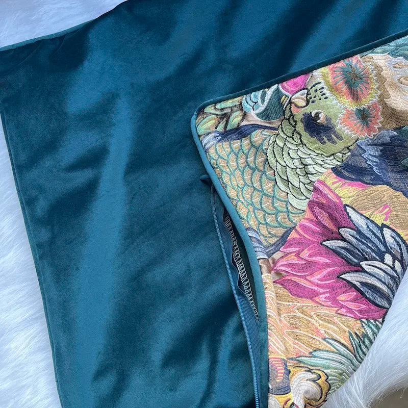 Housse de Coussin Bleu Canard et Beige avec un motif artistique de plusieurs oiseaux exotiques aux couleurs vibrantes et au style inspiré de la tapisserie classique, présenté sur un fond beige clair  - housse vide