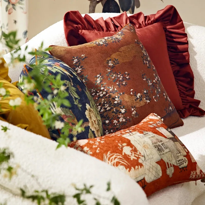 Housse de Coussin Fleur Japonais avec un motif floral traditionnel inspiré de l'Asie. Le coussin est marron avec des nuances plus claires et plus foncées créant un fond texturé. Le design présente des branches avec de petites fleurs blanches et des feuilles sombres dispersées sur le coussin. Le style général est élégant et classique - mis en scène sur canapé blanc