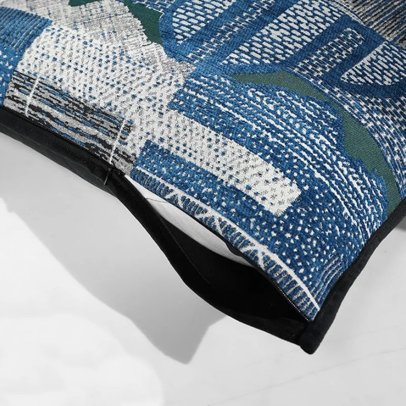 housse de coussin bleu et argent contemporain, avec un design abstrait tissé en bleu, blanc et vert, souligné par un passepoil noir. Fond uni blanc, idéal pour une présentation de produit - zoom sur matière