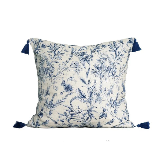 Housse de Coussin 45x45 Lin Blanc décoratif carré avec motifs floraux bleus sur fond blanc, agrémenté de pompons bleus aux quatre coins, présenté sur un arrière-plan clair et minimaliste - de face