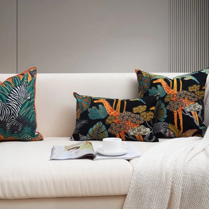 Housse de Coussin en Velours Jungle brodé avec une girafe orange et jaune, un zèbre noir et blanc, entourés de feuilles tropicales colorées sur un fond noir, style exotique et élégant - deuxième photo sur canapé blanc
