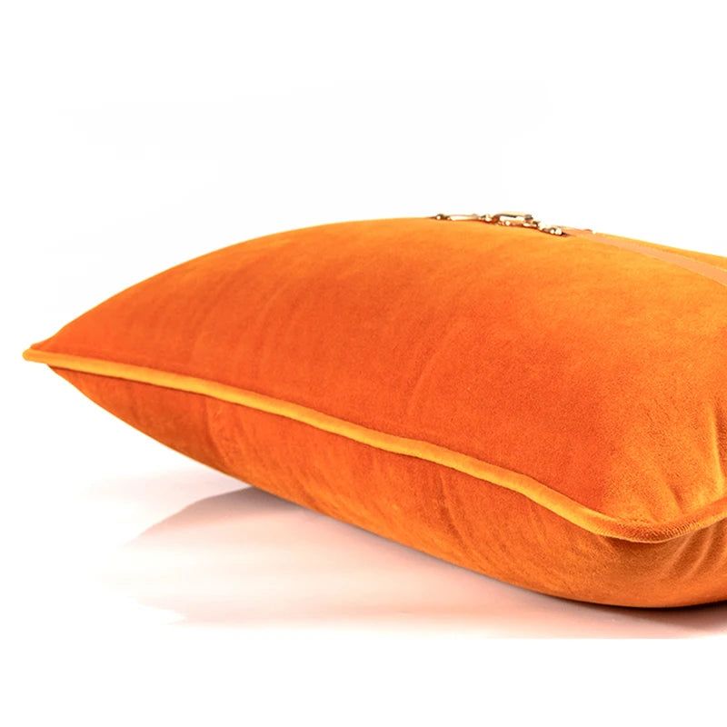 housse de coussin 30x50 orange rectangulaire en velours orange vif avec une bande horizontale en cuir marron clair ornée d'un détail métallique en forme de mors équestre - couché