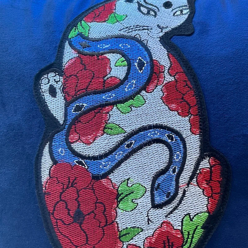 housse de coussin chat vintage en velours bleu profond avec une broderie artistique représentant un chat stylisé entouré de fleurs rouges et d'un serpent bleu, inspiré par l'art japonais traditionnel - zoom sur broderie