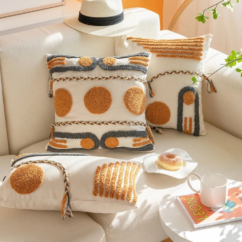 Housse de Coussin Style Boheme Terracotta décoratif au style bohème minimaliste, avec broderies en relief de formes géométriques jaunes moutarde et grises anthracite, sur fond blanc texturé. Bordures tressées artisanales - modèle 1 de face - plan d'ensemble sur canapé blanc