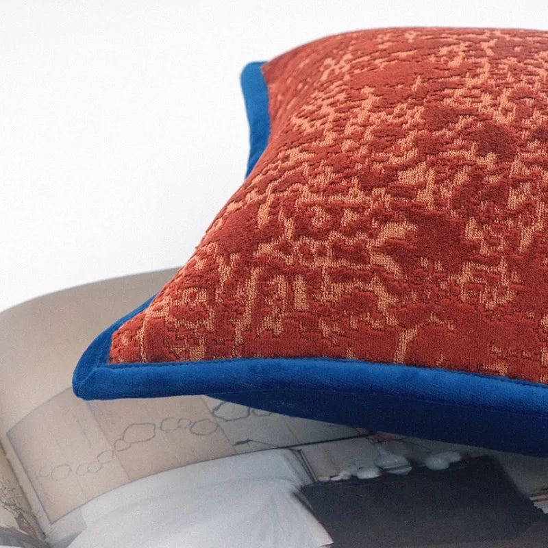 Coussin carré en tissu texturé rouge brique avec bordure bleue, motif irrégulier en relief. sur Fond blanc - zoom sur matière