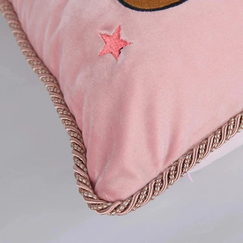 Coussin décoratif avec illustration fantaisiste d'un chat vêtu d'un pull bleu marine étoilé et d'une jupe rose à motif léopard, sur fond rose décoré d'étoiles colorées, avec une bordure torsadée beige et brune.- zoom sur passepoil