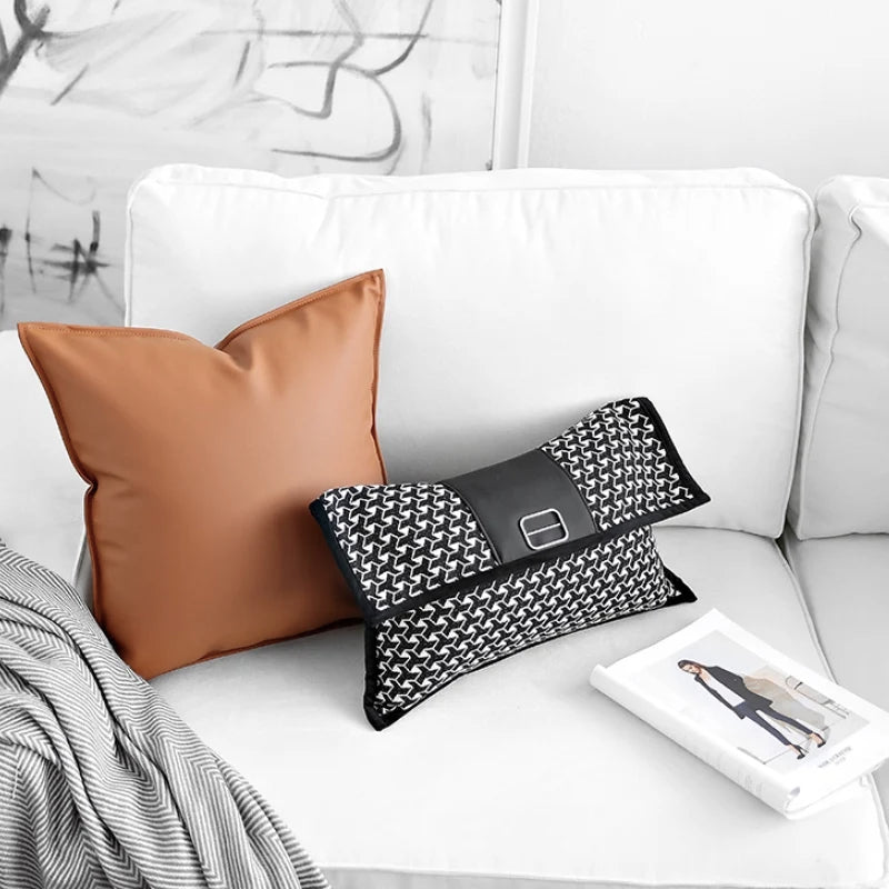 Housse de Coussin Rectangulaire Noir et Blanc En Forme de pochette élégante rectangulaire avec un motif en chevrons noir et blanc, un détail central en cuir noir et une boucle en métal argenté, posée sur un fond blanc minimaliste. - posée sur canapé blanc