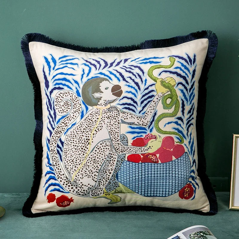 housse de coussin blanc avec dessin illustrant un singe blanc à pois noirs tenant un serpent vert à côté d'un panier rempli de grenades rouges, sur fond de motifs abstraits en bleu - sur fond bleu