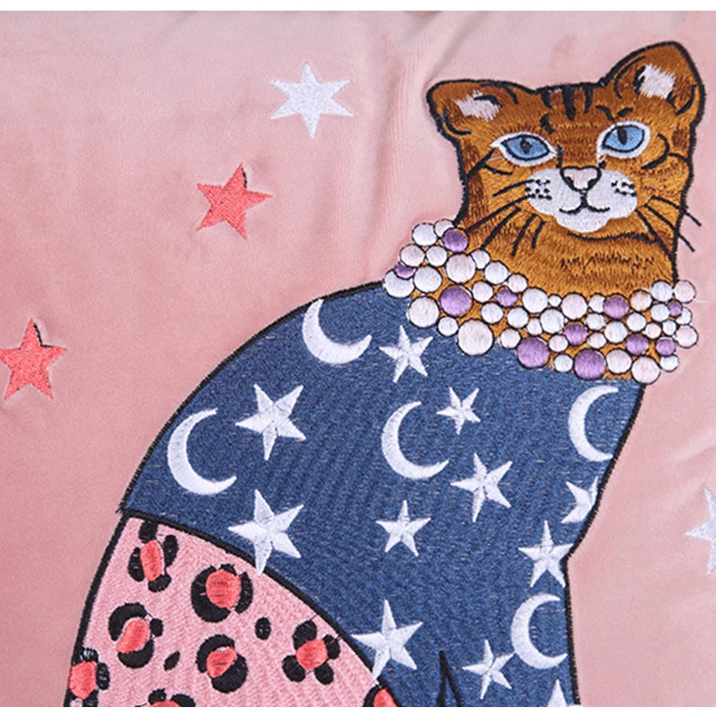 Coussin décoratif avec illustration fantaisiste d'un chat vêtu d'un pull bleu marine étoilé et d'une jupe rose à motif léopard, sur fond rose décoré d'étoiles colorées, avec une bordure torsadée beige et brune. - zoom sur broderie