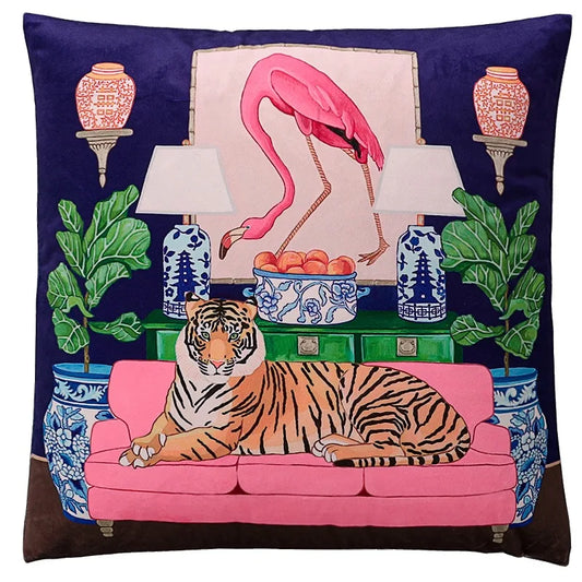 Housse de Coussin 60x60 Flamants Roses avec un design éclectique et artistique. Scène centrale comprenant un tigre couché sur un canapé rose vif, un flamant rose debout dans un cadre, entouré de vases chinois bleus et blancs, de lampes et de plantes exotiques sur un fond bleu marine - de face