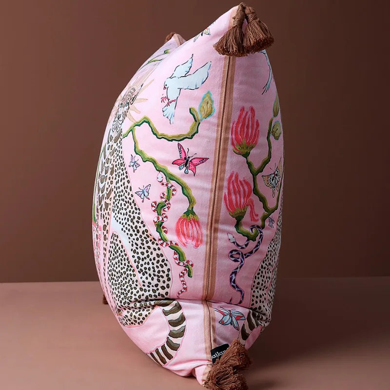 housse de coussin rose et vert illustratif avec deux guépards assis, fond rose, auréoles dorées, vase décoratif entre eux, éléments floraux, oiseaux blancs, papillons colorés, pompons marron aux coins - de coté