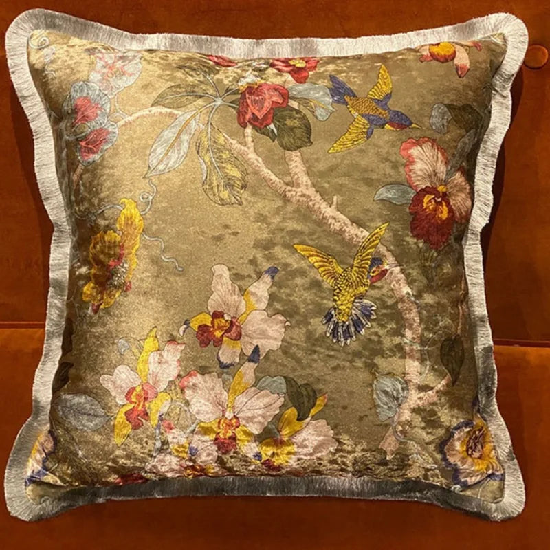 Housse de Coussin Boheme Fleur avec un fond beige et doré et des motifs floraux colorés, incluant des oiseaux colorés - de face et en scène sur canapé