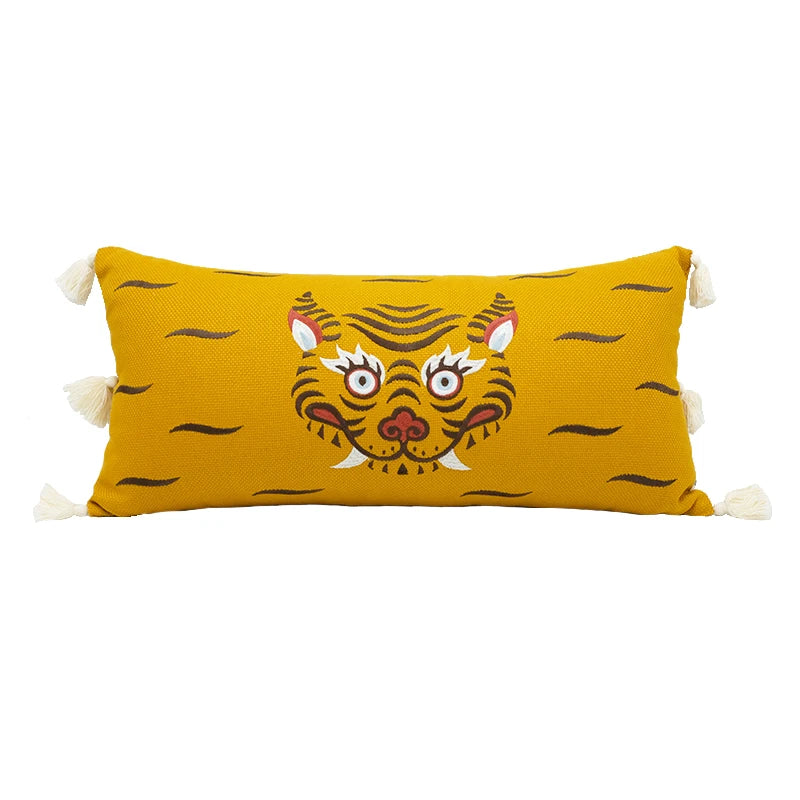 Housse de Coussin Rectangulaire Moutarde avec un motif central représentant un visage de tigre stylisé, orné de pompons blancs aux coins - de face