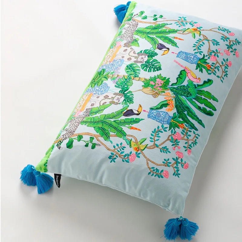 housse de coussin rectangulaire en velours avec motifs tropicaux avec des perroquets, des toucans, des léopards et des plantes luxuriantes, orné de pompons bleus - en plongée