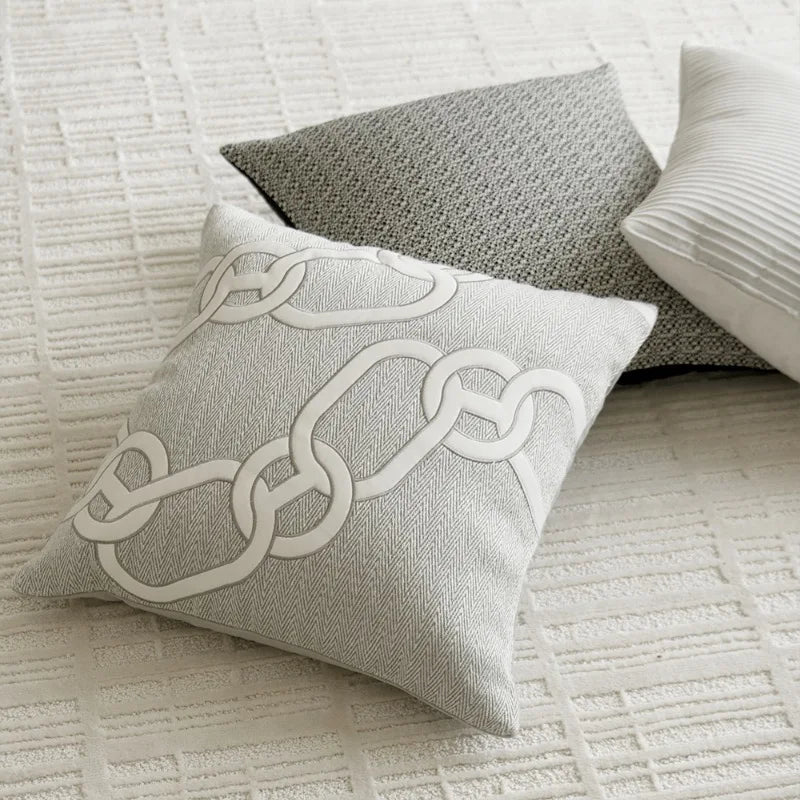 Housse de Coussin Couleur Blanc et gris clair avec motif de chaînes entrelacées blanches, sur fond à texture en chevrons - sur tapis blanc