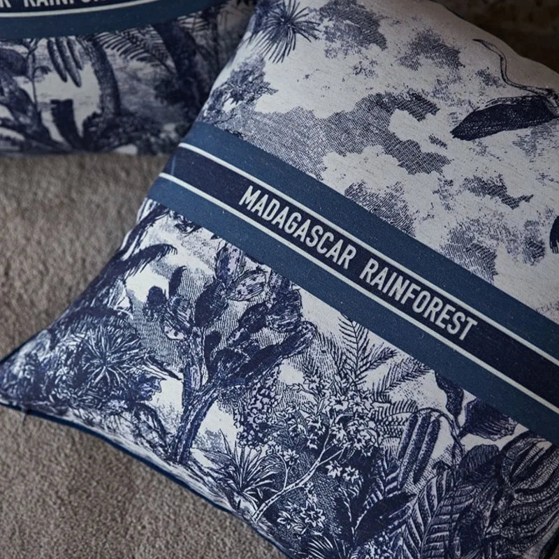 Housse de Coussin 45x45 avec Lettre représentant la forêt tropicale de Madagascar avec des palmiers, des flamants roses et un grand papillon. Le texte "MADAGASCAR RAINFOREST" est centré, encadré par deux lignes horizontales - zoom sur inscription